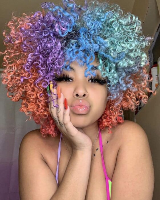 Chica con el cabello rizado y teñido de colores morado, naranja y verde