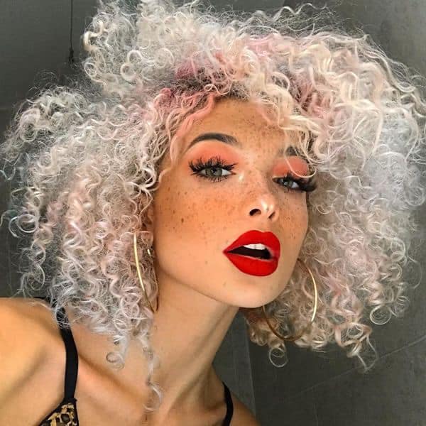 Chica con el cabello rizado y teñido de color platinado con la raíz rosa