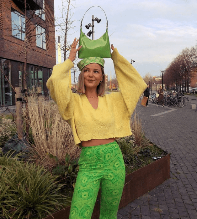 joven rubia con bolso verde pequeño, suéter amarillo holgado y leggings verdes brillantes