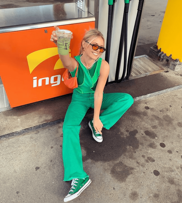 joven rubia con gafas de sol cafés, top verde, overol verde brillante y zapatillas converse verdes