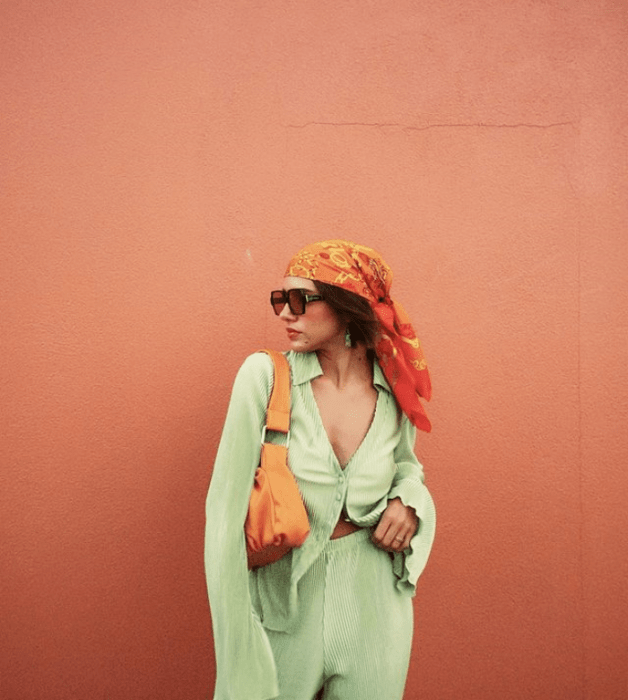 joven de cabello oscuro con gafas de sol oscuras, blusa verde pistache, pantalones holgados pistache y bolso naranja de piel