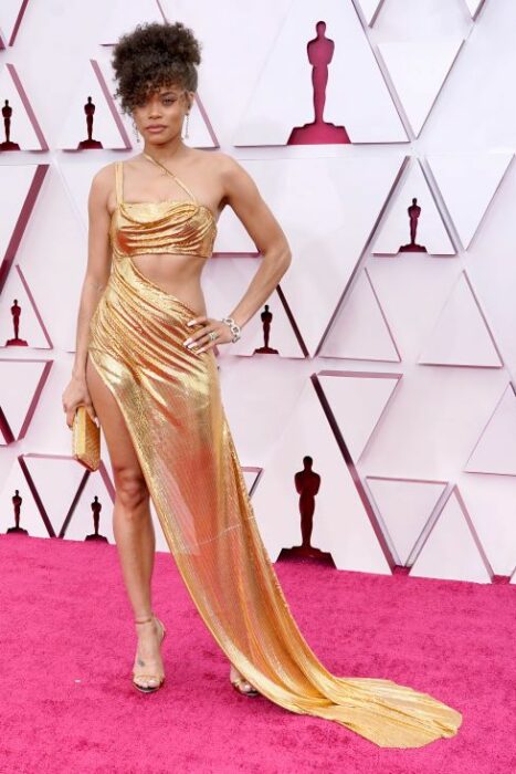 Andra Day en la alfombra roja de los Oscar usando un vestido de color dorado