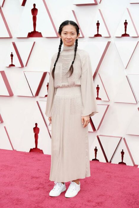 Chloé Zhao usando un vestido de color rosa con dos trenzas y tenis