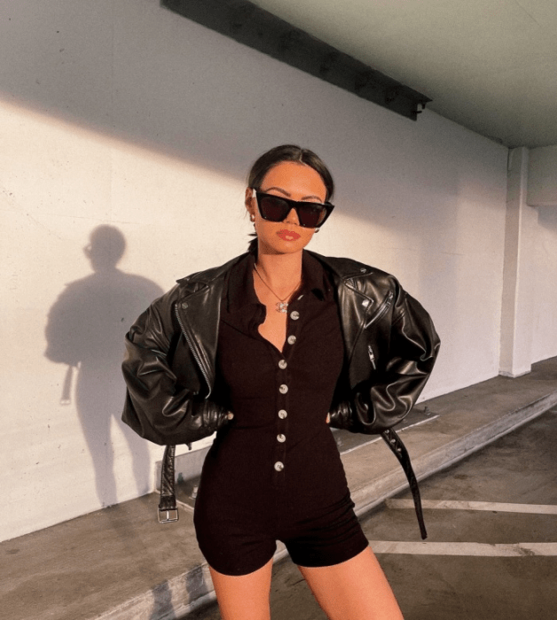 chica de cabello oscuro con lentes de sol, jumpsuit negro de botones al frente, chamarra de cuero