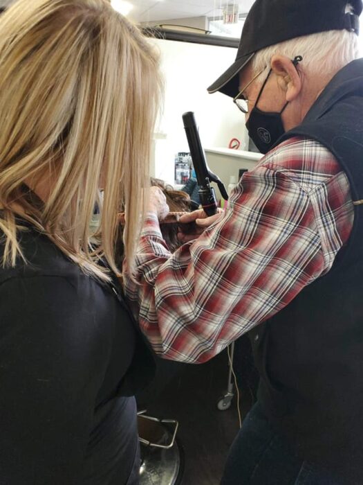 Abuelito sujetando una pinza para rizos mientras practica con una muñeca de peinados