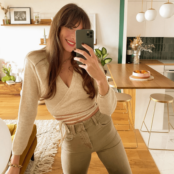 chica de cabello oscuro usando una blusa color beige de manga larga con tirantes en la cintura y jeans claros ajustados