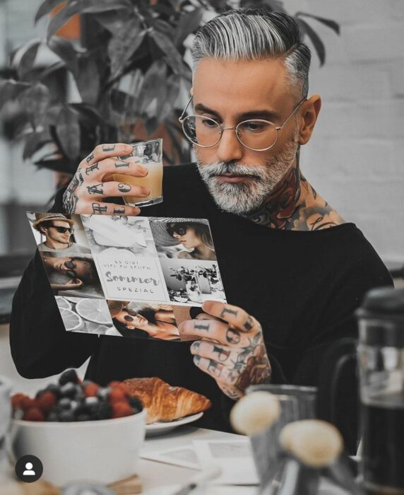 Hombre con tatuajes disfrutando de un desayuno mientras hojea una revista