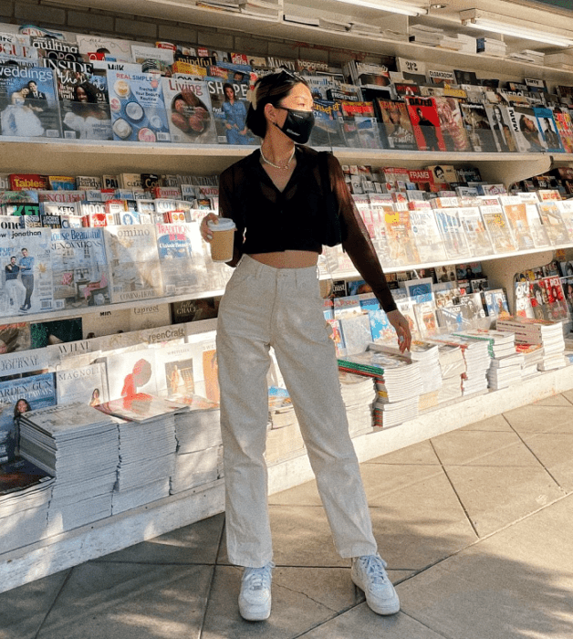 chica de cabello negro usando un crop top café de manga larga, pantalones blancos, tenis blancos