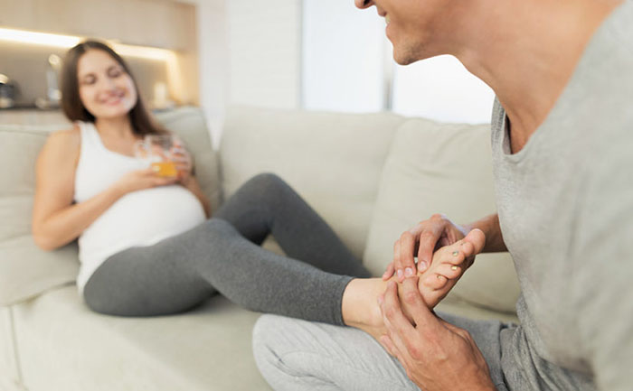 Mujer recibiendo un masaje de pies mientras está recostada en un sofá