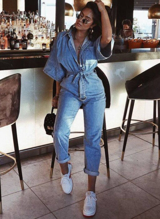 Chica usando un jumpsuit de color mezclilla con tenis blancos