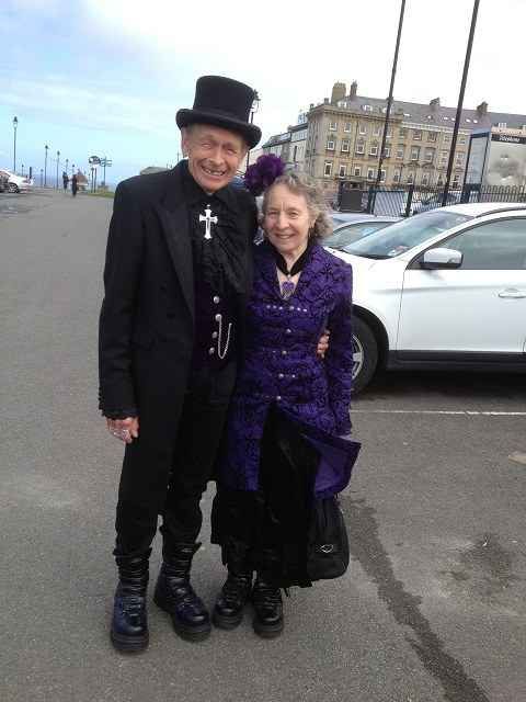 Mujer de la tercera edad vestida de color negro junto a su esposo también vestido de negro 