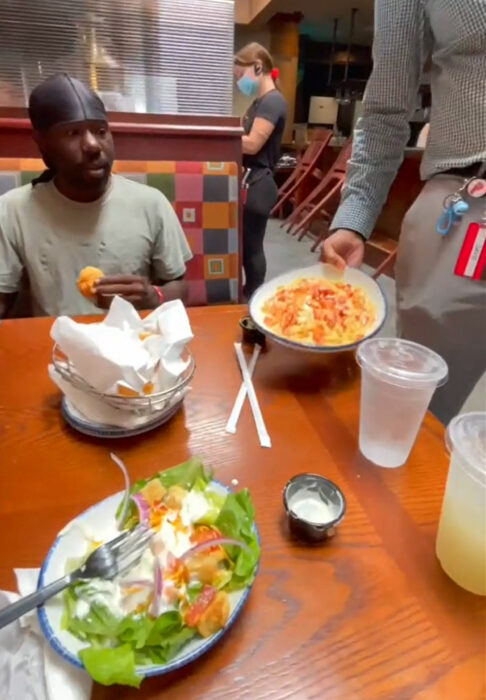 Hombre sin hogar comiendo en un restaurante junto a varias personas