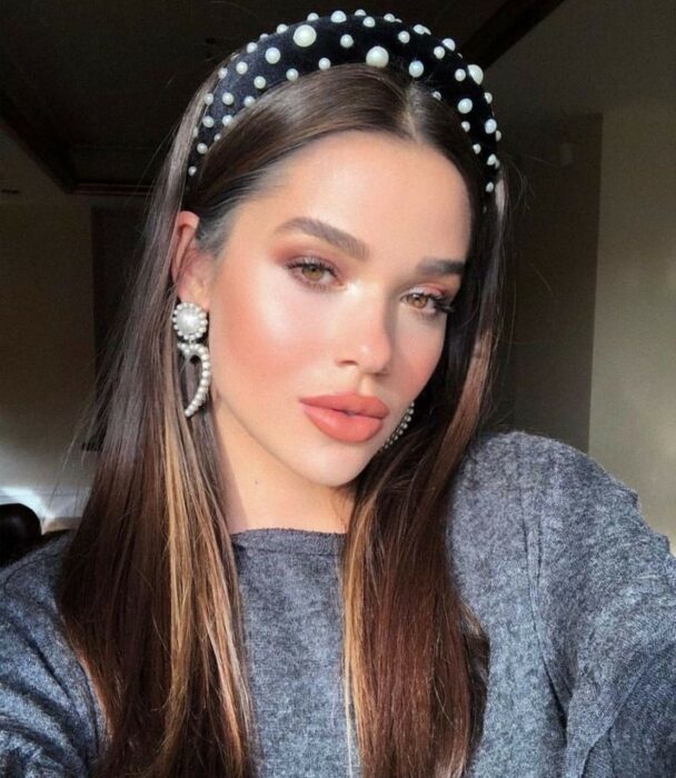 Chica con el cabello hasta los hombros sujetado con una diadema negra y perlas