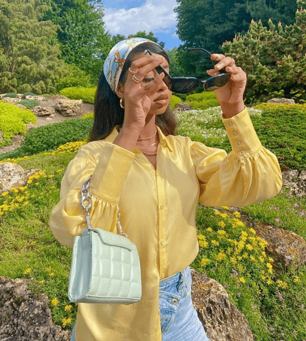 chica morena con lentes de sol negros, blusa amarilla con mangas abombadas, jeans a la cintura con bolso celeste