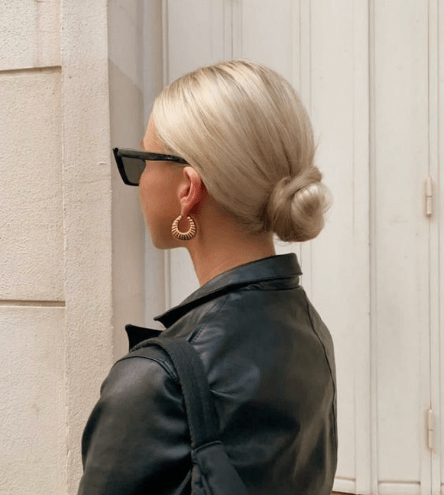mujer platinada con chongo bajo, gafas de sol negras y chaqueta de cuero negro
