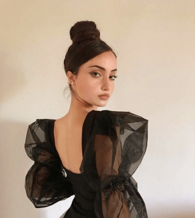 mujer de cabello negro con un chongo alto, blusa semitransparente negra y mangas abombadas