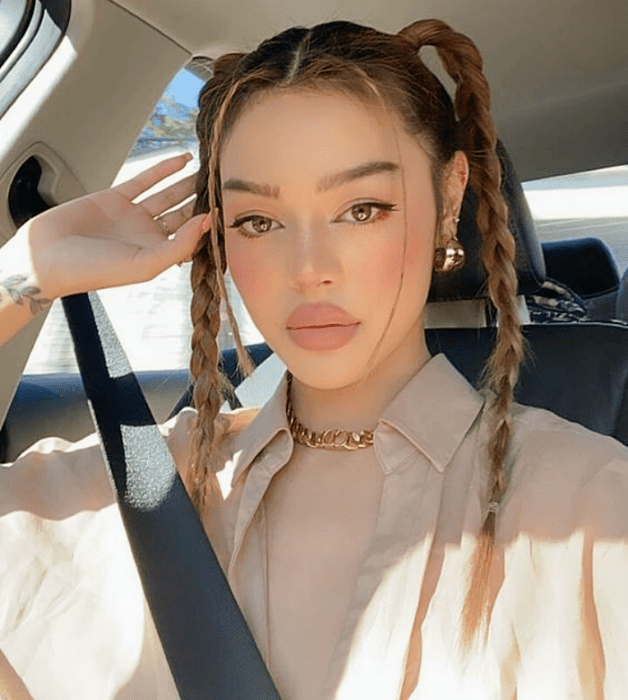 mujer de cabello claro con trenzas altas, blusa beige y top beige