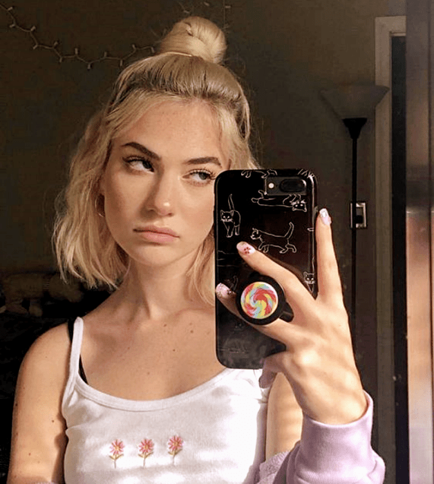 mujer rubia con cabello corto, medio chongo y top blanco de tirantes