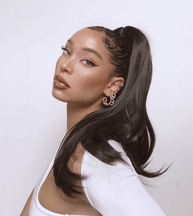 mujer de cabello oscuro con una coleta alta al estilo de los 90 y un top blanco de manga larga