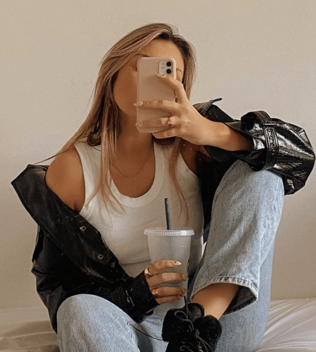 chica rubia usando un top blanco de tirantes, chamarra de cuero, jeans ajustados, botines negros