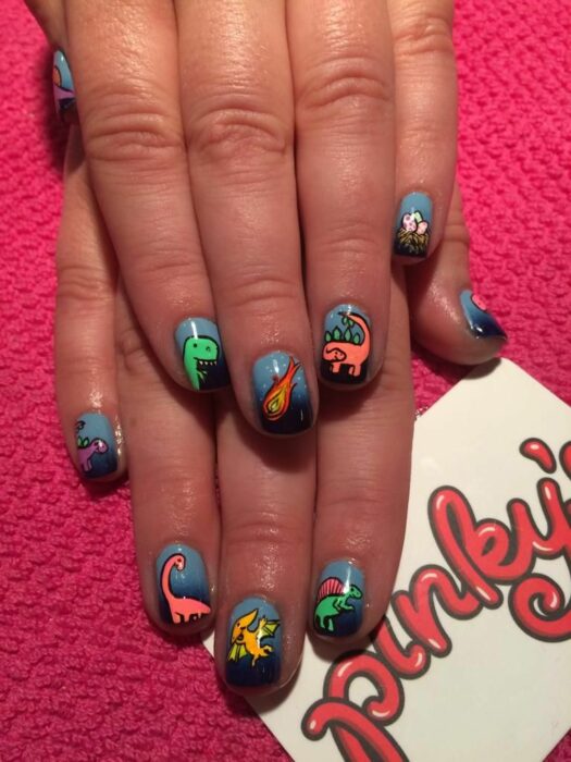 Chica con un diseño de uñas de dinosaurios en diferentes colores