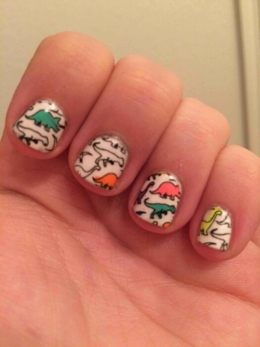 Chica con un diseño de uñas de dinosaurios en diferentes colores