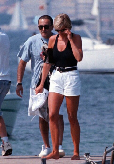Diana Spencer usando unos shorts de color blanco con una blusa top de color negro mientras camina por un puerto