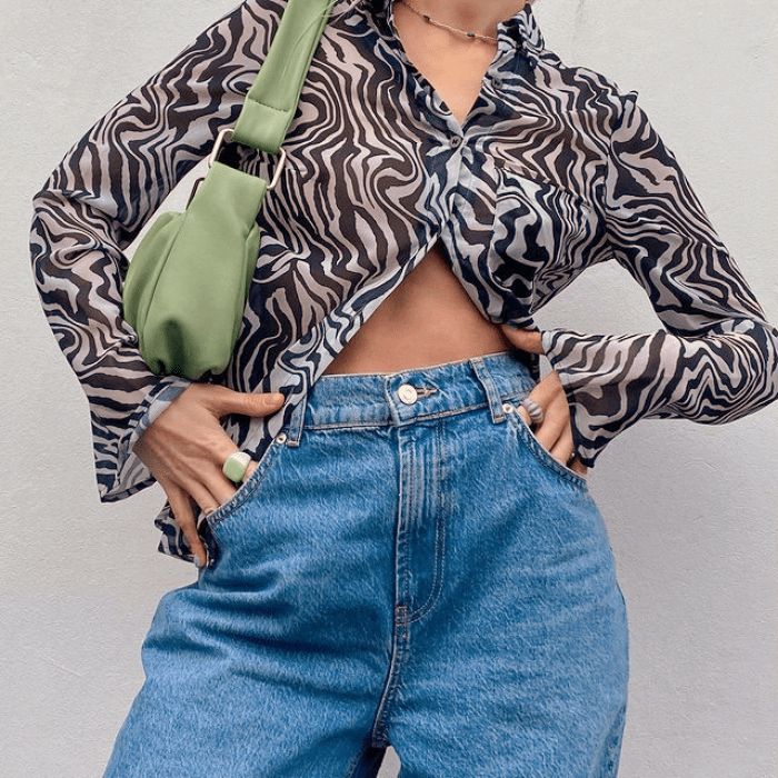 blusa semitransparente de cebra con botones al frente y manga larga, jeans a la cintura y bolso pequeño de cuero verde claro