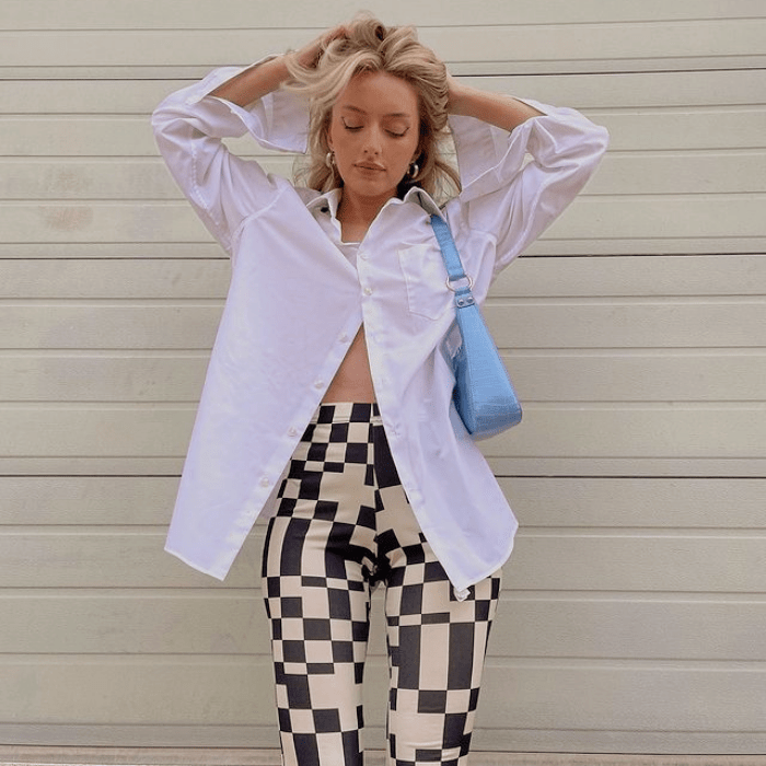 chica rubia con camisa oversized blanca, pantalones blancos con cuadros cafés y bolso pequeño azul de cuero
