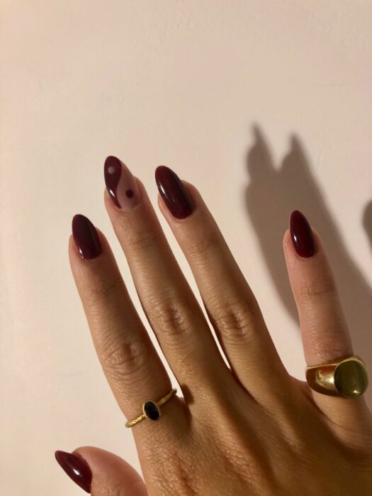 Chica mostrando sus uñas con diseño Yin Yang en color guinda con nude