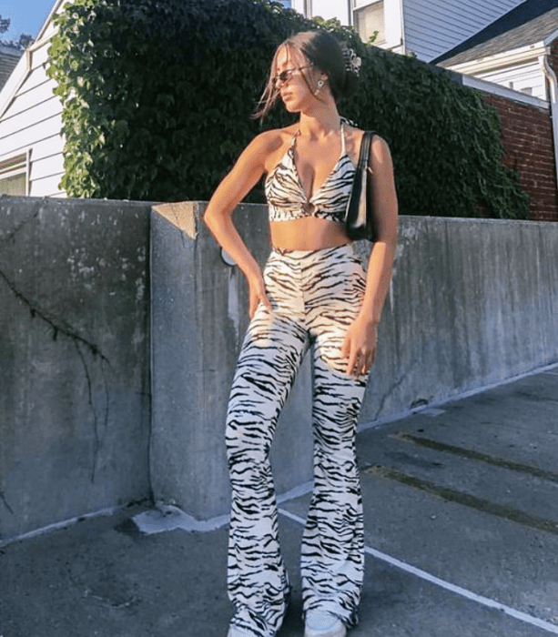 chica de cabello claro usando lentes de sol, crop top de cebra, pantalones a la cintura de cebra acampanados y bolso negro de cuero