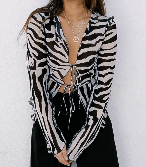 chica de cabello oscuro usando una blusa de cebra con manga larga, abierta de en medio con escote pronunciado y jeans negros ajustados