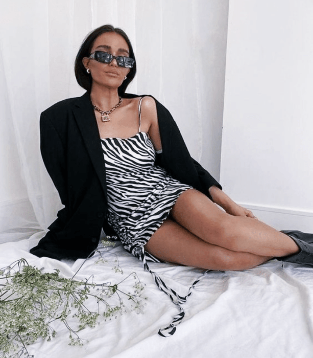 chica de cabello oscuro usando lentes de sol, vestido de cebra de tirantes, abrigo negro, botines negros de cuero