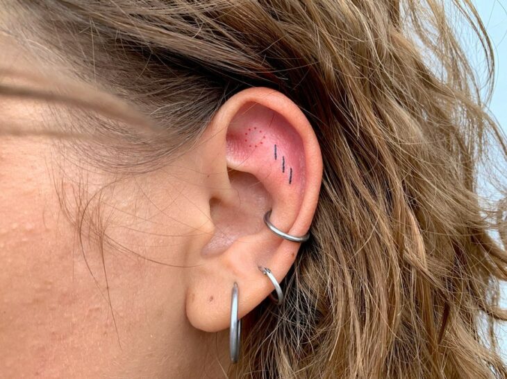 Chica con un tatuaje en la oreja en forma de pequeñas líneas de colores