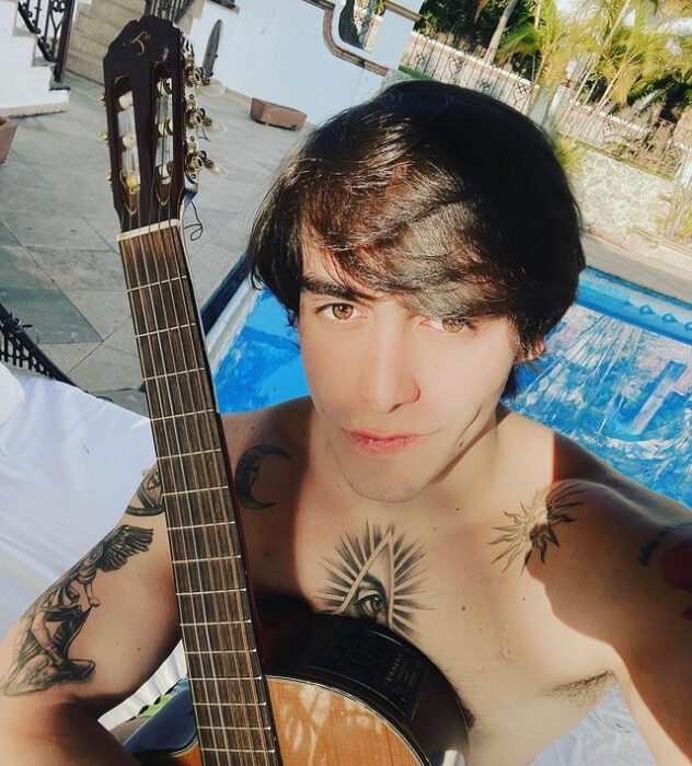 Julián Figueroa sentado frente a una piscina tomando el sol y sosteniendo su guitarra