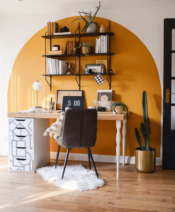 oficina blanca con acento amarillo, estanterías delgadas, silla negra, escritorio de madera y plantas
