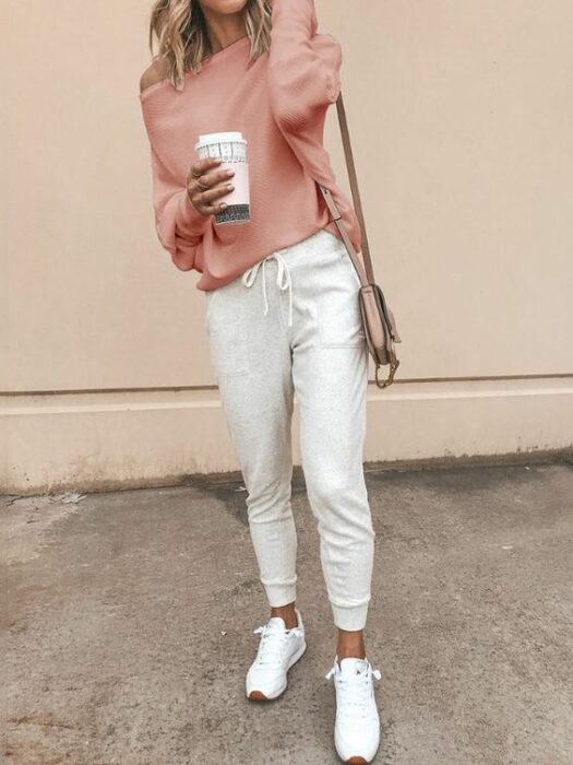 Chica usando una blusa rosa, chándal color beige y tenis blancos