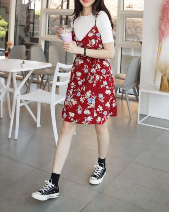 Chica usando un vestido rojo con estampado de flores en colores claros, con una blusa blanca debajo y converse negros