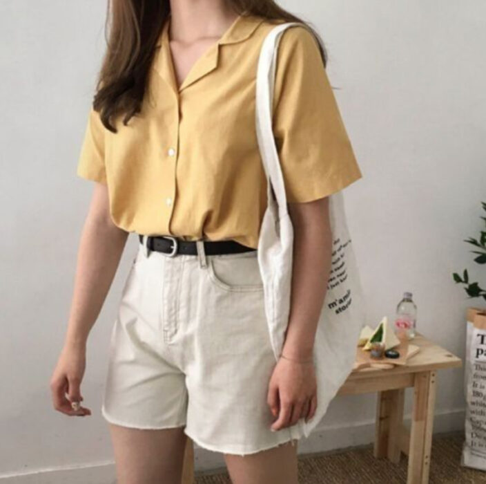 Chica usando camisa amarilla, con short beige y cinturón negro