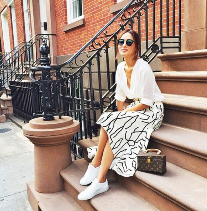 Chica usando camisa blanca, falda del mismo color con detalles negros y tenis blancos