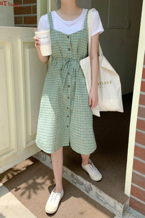 Chica usando un vestido largo de tirantes verdes con cuadros blancos, camiseta blanca de manga larga debajo y tenis blancos