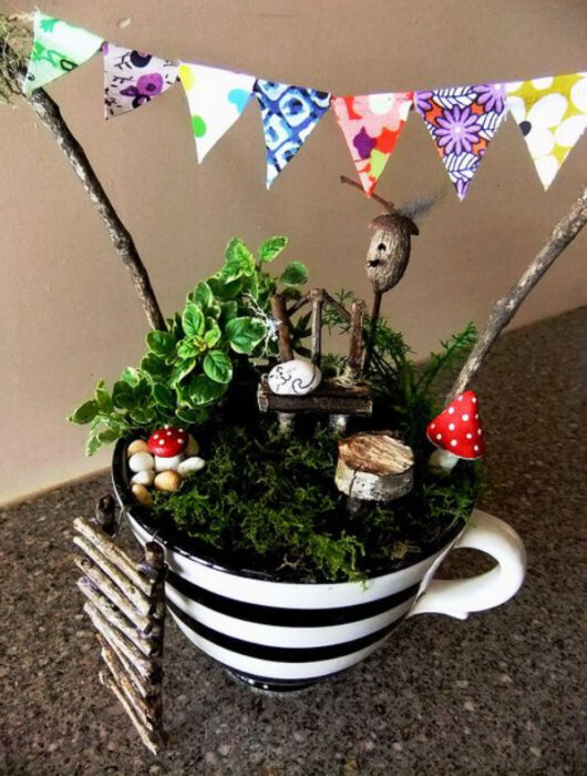 Mini jardín en taza con diseño de rayas en blanco y negro con varias plantas y decoraciones del bosque