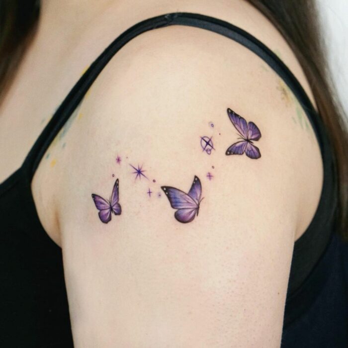 Tatuaje con tres mariposas miniatura en tonos morados revoloteando; 15 Bellos tatuajes con mariposas para iniciar una metamorfosis