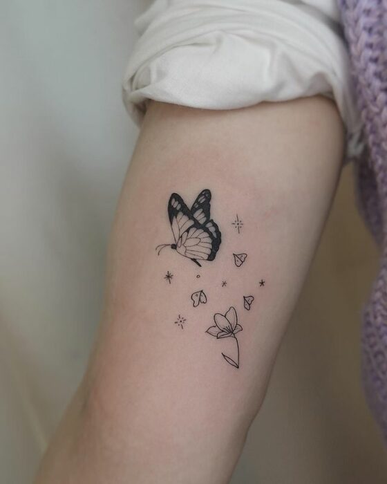 Minitatuaje de mariposa en color negro sobrevolando unas flores; 15 Bellos tatuajes con mariposas para iniciar una metamorfosis