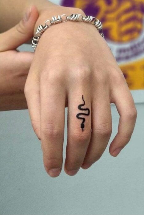 Chica con un tatuaje en forma de serpiente en el dedo medio