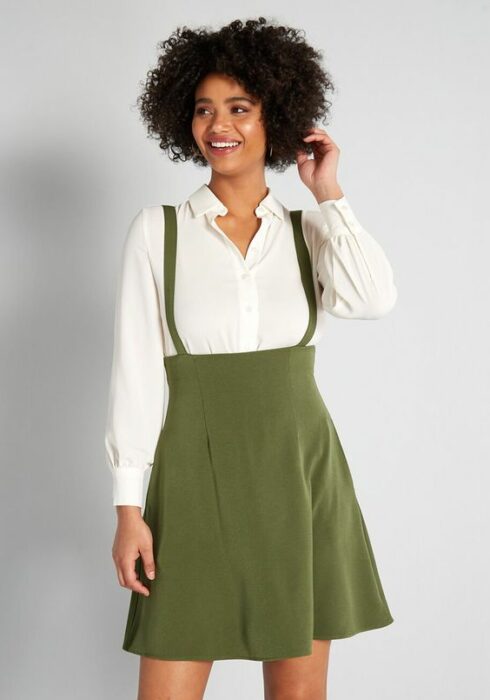 Chica de cabello rizado, usando camisa blanca con jumper color verde