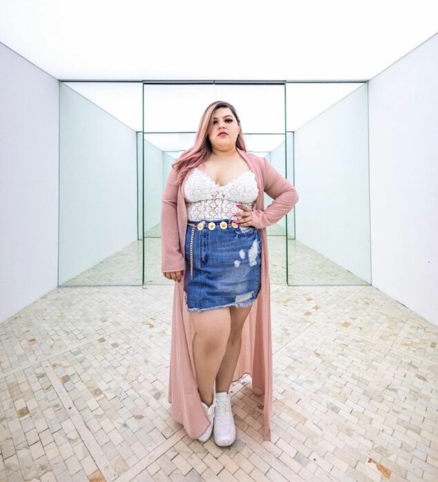 Priscila Arias la Fatshionista usando una falda de jean, top blanco, botas blancas y un conjunto rosa mientras modela