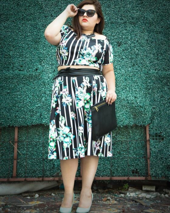 Priscila Arias la Fatshionista posando para una foto mientras usa un vestido de color verde con estampado en blanco y un clutch negro