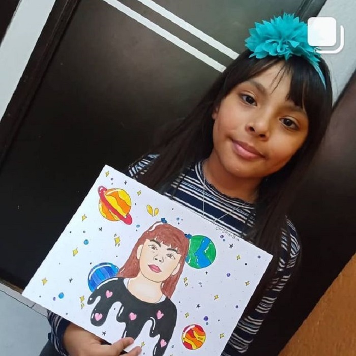 Adhara Pérez mostrando un dibujo de ella y los planetas