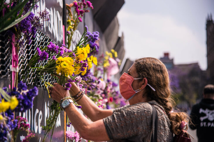 Mujer colocando flores sobre una valla colocada para frenar las marchas del 8 de marzo 2021